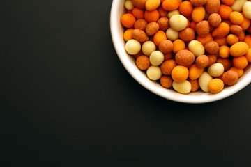 Peanuts with a crispy crust around it in a white bowl on a black metallic surface. Copy space for text.