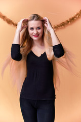 Obraz premium Portrait of a cute girl in a black T-shirt with long beautiful hair and great makeup. Concept of a young blonde woman with New Year's decor. Smiling, showing emotions on a pink background.