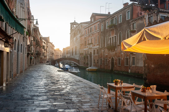 Fototapeta Venetian channel in the morning. Embankment and a street cafe in the light of the rising sun