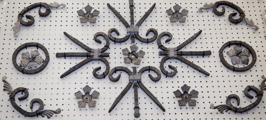 Forged metal products in the form of curls, circles, flowers, leaves fixed on a white stand. Construction, repair, art,  design.