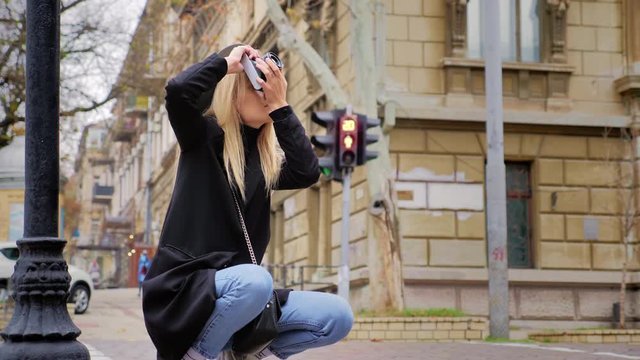 A young Caucasian hipster woman takes a picture on a vintage retro film camera. Crossroads road and traffic lights in the background. The concept of street photography on film equipment.
