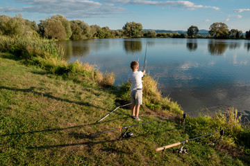 Boy fishing on a lake. Beautiful fish pond in Badin, near Banska Bystrica, Slovakia. Shining sun over the fish pond in summer day. Child holding fishing rod and catching fish. Little fisherman.