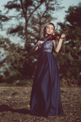 face of a beautiful girl with a violin under her chin outdoors, young woman playing a musical instrument on nature in solitude, concept music and feelings