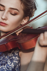 face of a beautiful girl with a violin under her chin outdoors, young woman playing a musical...
