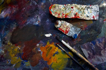 Artist's palette with oil paints and brushes, soft focus. Artistic paintbrushes, paints and palette knife on an old wooden palette, view from above.