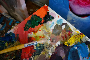 Artist's palette with oil paints and brushes, soft focus. Artistic paintbrushes, paints and palette knife on an old wooden palette, view from above.