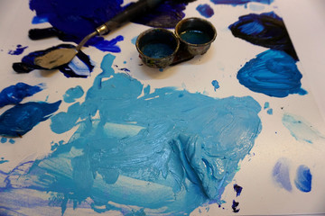Close up of spots of blue oil colors on a painter s pallete with knife and containers. Cold colors harmony on a plastic pallete.