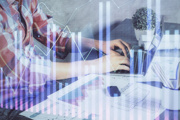 Double exposure of stock graph with businessman typing on computer in office on background. Concept of hard work.