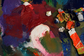 Artist's palette with oil paints and brushes, soft focus. Artistic paintbrushes, paints and palette knife on an old wooden palette, view from above.