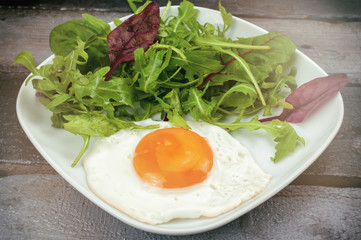 Fried egg with mixed salad on wooden table.