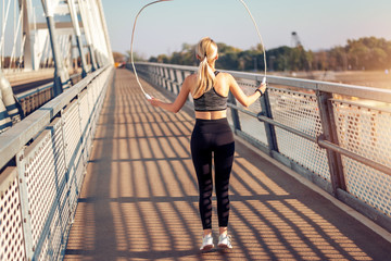 Adult woman skipping the rope on the bridge.