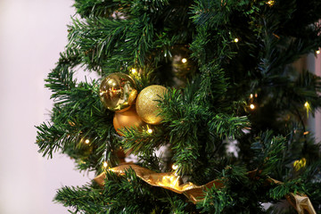 Traditional decorated baubles hangs on green twigs tree of pine. Bright gold balls on Christmas tree of fir or spruce with string rice lights bulbs. Ornaments to christmas celebration, holiday scene.