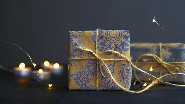 Gift in beautiful paper and tied with a felt ribbon. Candles are burning in the background. Festive Christmas atmosphere. Gifts and party lights. High quality 4K video.