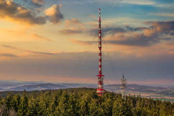 Telecommunications tower, antenna and satellite dish over Sumava forest.