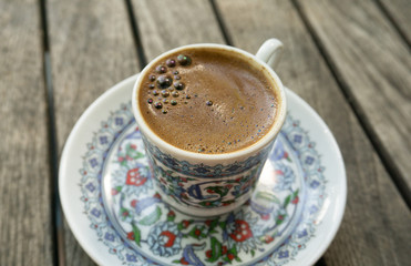 Cup of coffee with foam on a wooden table close-up. Traditional black Turkish coffee in a beautiful Cup with national patterns.