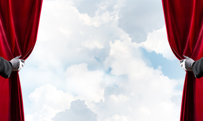 Cloudy landscape behind red curtain and hand holding it