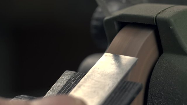 a carpenter grinds a chisel on a grinder. macro 4k