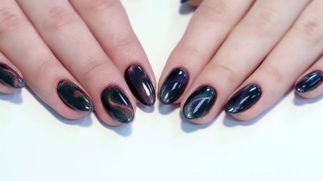 Closeup top view of professional colorful glossy brilliant holiday manicure at fingernails of young woman. Modern trendy shiny amazing cat eye effect nails design. Real time 4k video footage.