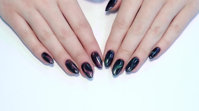 Closeup top view of professional colorful glossy brilliant Christmas holiday manicure at fingers of young woman. Modern trendy shiny amazing cat eye effect nail design. Real time 4k video footage.