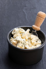 Potted aged Blue stilton cheese on black stone background