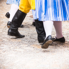 Closeup of legs of little girl in striped white blue skirt and small school boy in high black dancing leather boots and period costume yellow trousers perform folklore dances in Cesky Krumlov - UNESCO