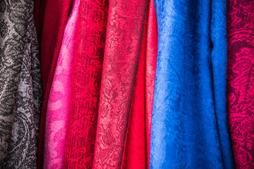 Fabric material background of woolen and cashmere scarfs and textured textile fabrics in fuchsia pink, warm berry red, burgundy to magenta purple and sky blue and gray black color.
