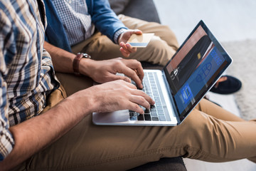 cropped view of jewish father using laptop with booking website and son holding credit card