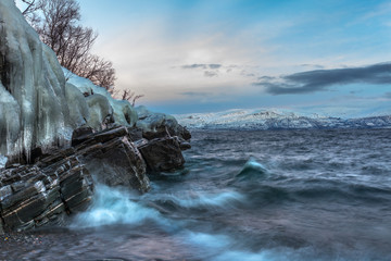 Icicles hanging from the rocks on the shore Tornetrask, Sweden. Polar night. long shutter speed