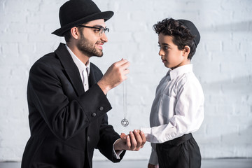 side view of smiling jewish father giving star of david necklace to son