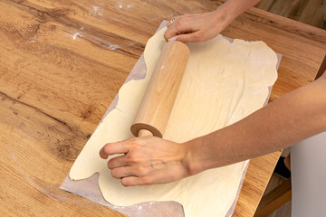 Sheeting dough. Women's hands are holding rolling pin and floured. Hands baking dough with rolling...