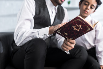 cropped view of jewish father and son reading tanakh in apartment