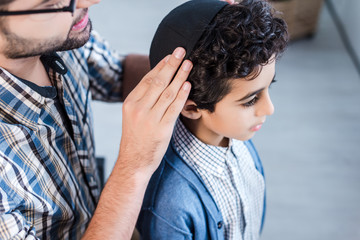 cropped view of jewish father wearing hat on son in apartment