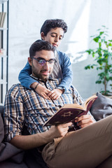 smiling jewish father and son reading tanakh in apartment