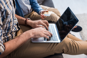cropped view of jewish father using laptop and son holding credit card in apartment