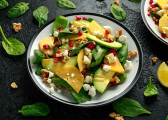 Persimmon, avocado salad with spinach, feta cheese, walnuts and pomegranate seeds. Healthy food.