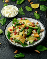 Persimmon, avocado salad with spinach, feta cheese, walnuts and pomegranate seeds. Healthy food.