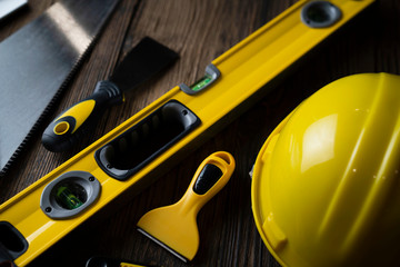 Contractor concept. Yellow hardhat, libella and other tools on the rustic wooden background.