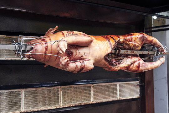 Cochinillo ensartado asado en horno de fuego girando.