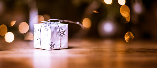 Close up of a gift box and fairy lights near decorated christmas tree over wooden floor background with lights and copy space