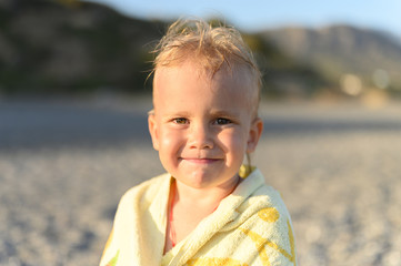 dreamy three year old little boy resting on the sea beach after swimming during the Golden hour