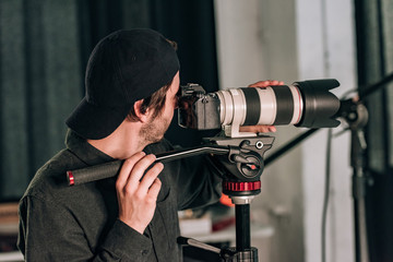 Side view of handsome videographer with camera on tripod in photo studio