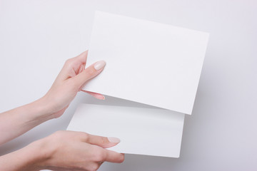Obraz premium Hand holds A5 paper for presentation or design insert. Minimalistic style on a gray background. Mock up