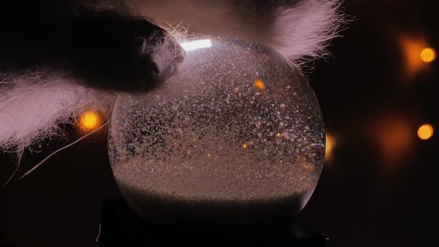 Christmas snow globe animation on hand. A garland of lights glows in the background.