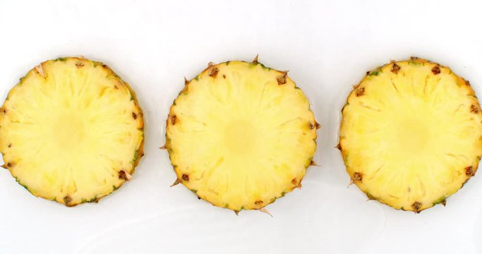 Water splashes in slow motion. Top view: three slices of sweet pineapple washed with water on a white background.