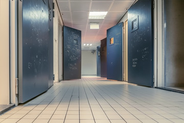 AMSTERDAM/NETHERLANDS-FEBRUARY 24: An empty corridor of a prison with tiles on the floor and open steel cell doors on which texts are scratched - 312213533