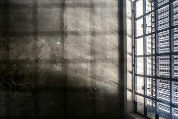 The very sober interior of a prison cell: barred windows with little light coming in and bare concrete walls - 312213580