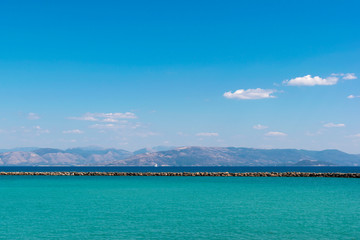 Obraz premium Colorful seascape. The bicolor sea is aquamarine and classic blue, the coastline of mainland Greece and the bright blue sky. Lefkimmi Port, Ionian Islands, Corfu, Greece. Space for text, quotes.