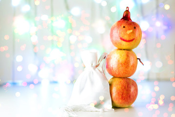 Concept of vegan Christmas, healthy food on holidays. Creative snowman from apples with bag gift standing on bokeh christmas light background. Merry Christmas and happy New Year greeting card.