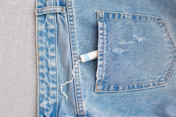 white female menstrual swab with a rope in the back pocket of jeans on a silver gray background