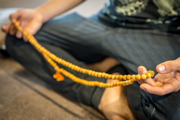 A male sitting in a meditation pose while holding meditation japa or mala beads, getting ready for...